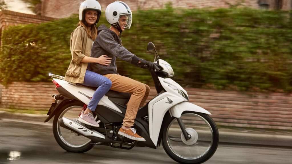 Una pareja de adolescentes se transportan en una Honda Wave blanca
