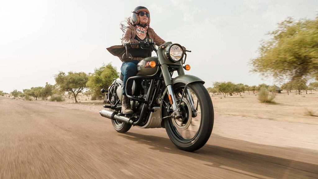 Una mujer sobre una Royal Enfield Classic 350 verde oliva se desplaza por una ruta