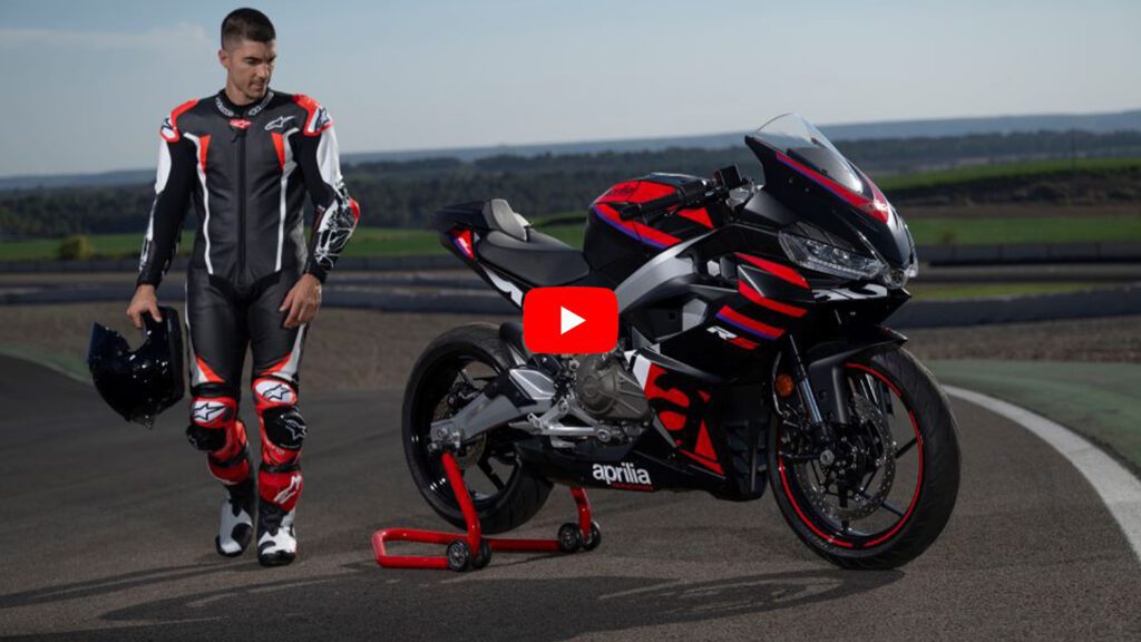 Un piloto con casco en la mano rodea a una Aprilia RS457 antes de subirse