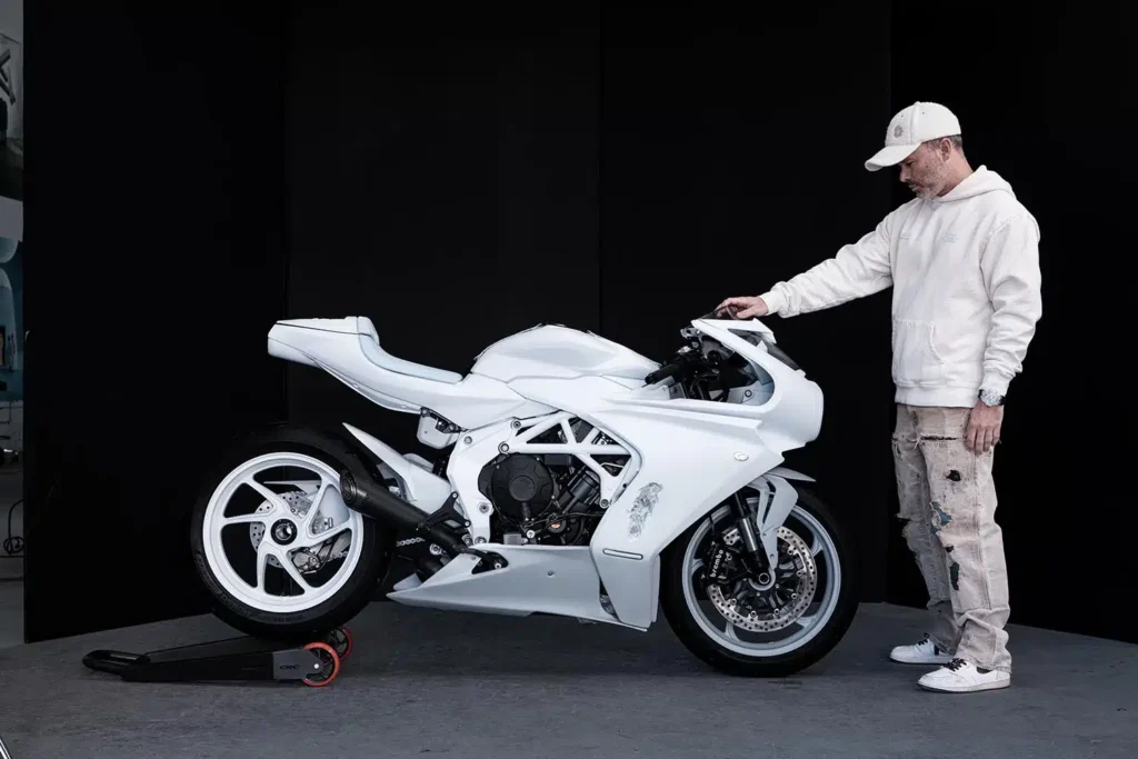 Un usuario vestido de blanco mira a su moto del mismo tono sosteniéndola del manillar