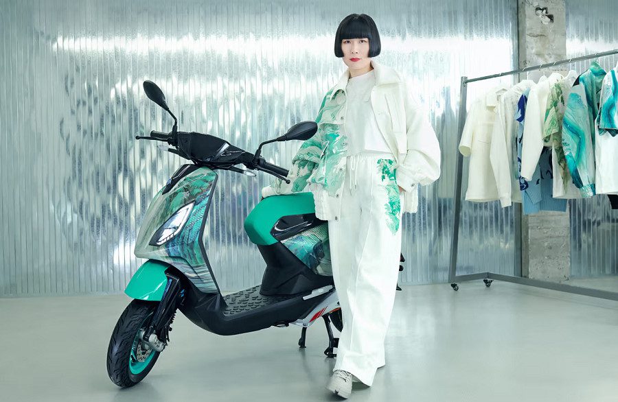 La artista china Feng Chen Wang posa junto a sus obra: el Piaggio 1 FWC Active y la ropa temática