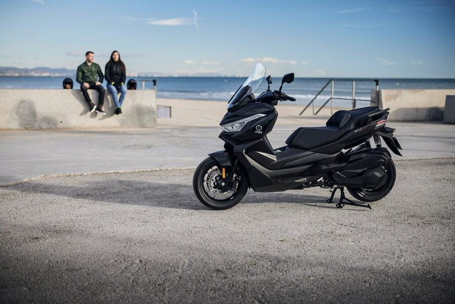 Una pareja sentada en una escollera marina conversan al lado de una Los dueños de un SR4 Max T oscuro