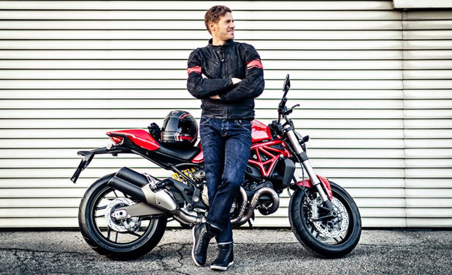 Joven sonriente apoyado sobre su nueva moto naked 