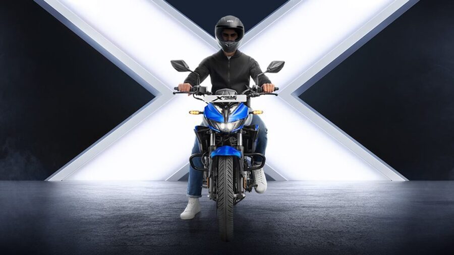 Una Xtreme 125 R de frente con su conductor sobre la moto y una gran equis de fondo