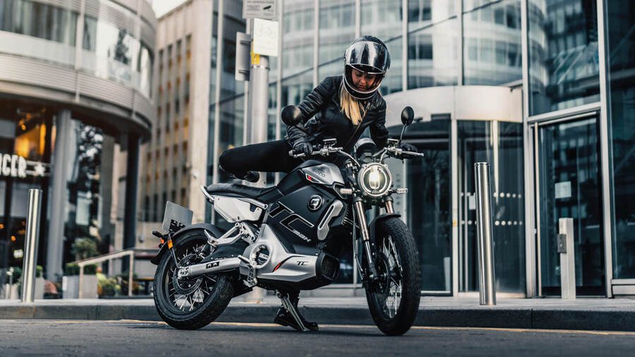 Una mujer se sube a una Super Soco TC Max negra y gris Una mujer se sube a una Super Soco TC Max negra y gris