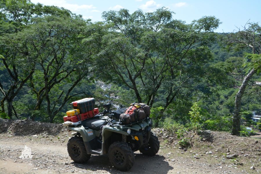 Escapada en ATV a los bosques montañosos de Catamarca Un ATV cargado de equipaje parado al borde de un camino con un frondoso bosque al fondo