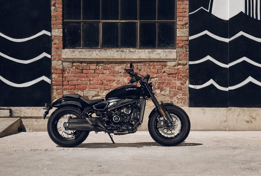 CFMoto 450CL-C totalmente negra para frente a un edificio de ladrillos con portones negros con ondas blancas.