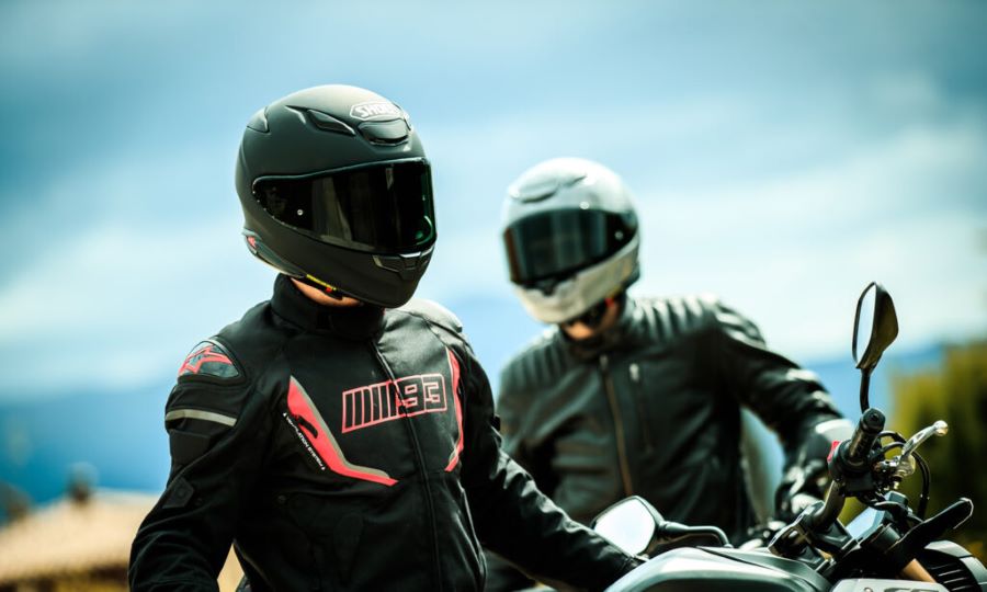 Dos pilotos, uno con casco negro Shoei NXR 2 y la leyenda "MM93" en la campera, esperan sobre sus motos deportivas.