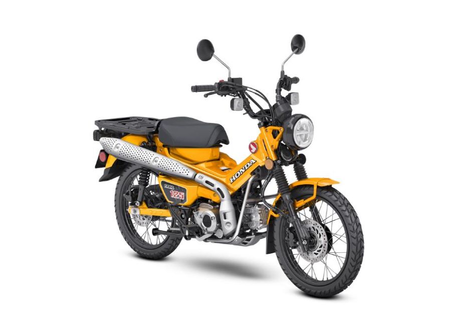 Una Honda Trail 125 de color amarillo cúrcuma luce su característico escape largo y ascendente.