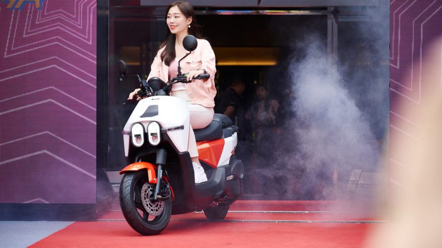Kymco-Dollar-presentación Una mujer de origen taiwanés sonríe sobre un Kymco Dollar.