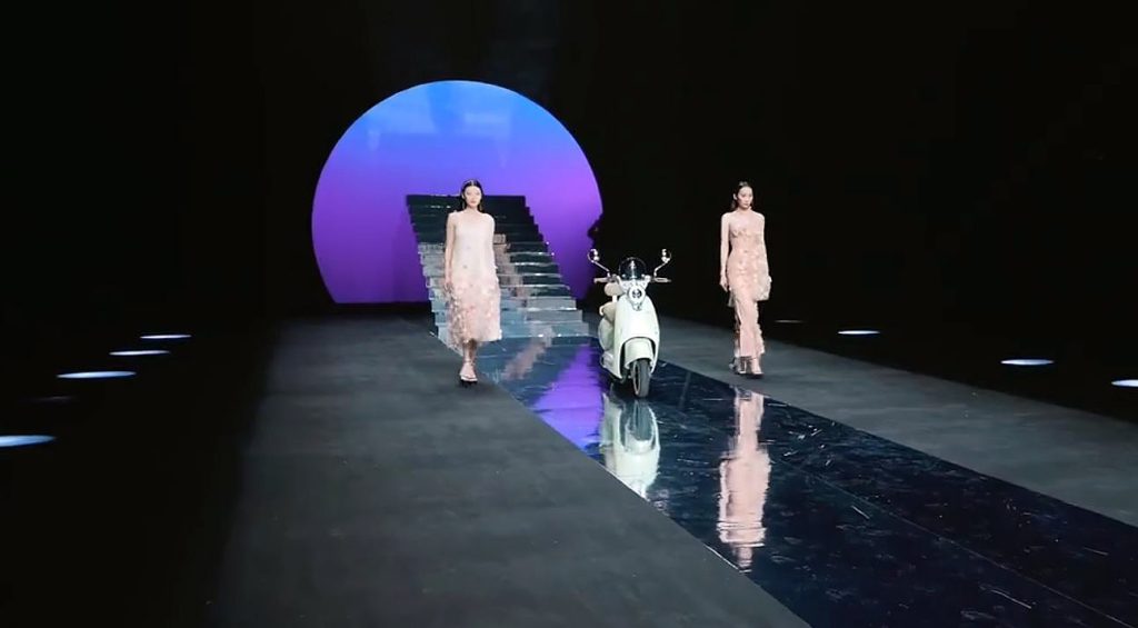 Un Scooter autónomo YADEA desfila entre dos modelos chinas