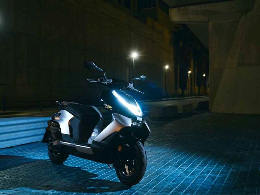 Zeeho AE8 S+ blanco, con las luces encendidas, posa en una explanada apenas bañada con una luz azul.