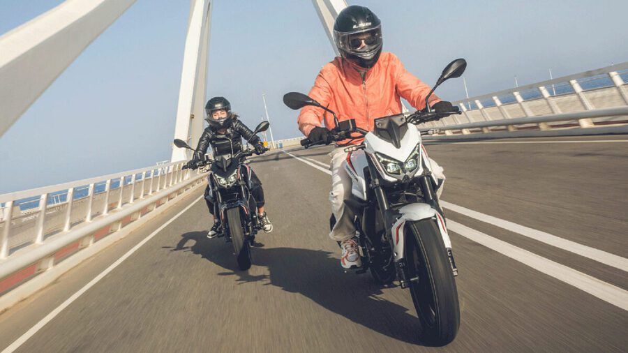  Dos TRX 125, una blanca y una negra. avanzan de frente sobre un puente.