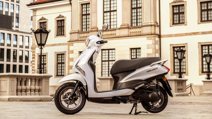 Un Yamaha D’elight 125 2024 blanco apostado frente a una edificio antiguo.