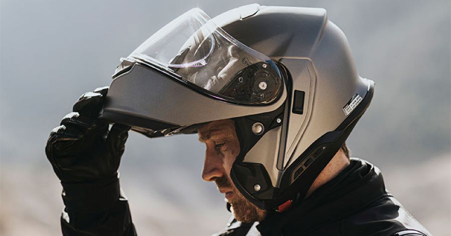 Un usuario se levanta la mentonera de una casco integral gris mientras realiza el SHOEI Ride & Test.