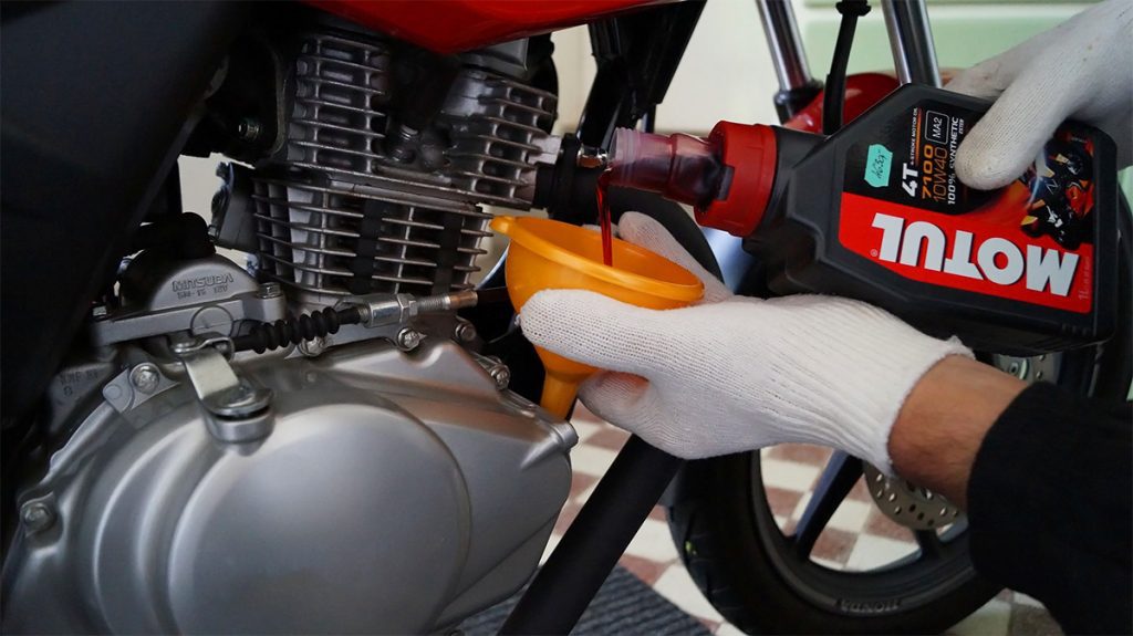una mano vierte aceite de un envase a un tanque de moto