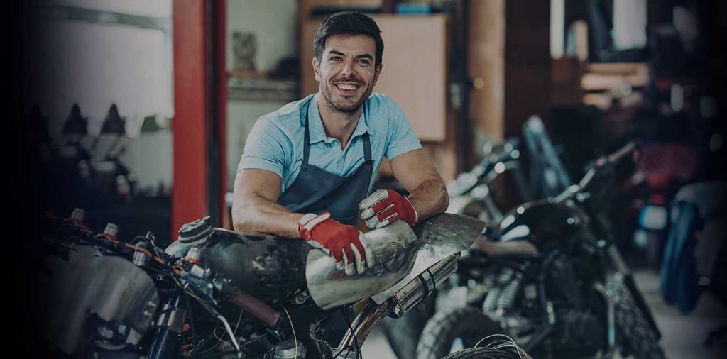 Un mecánico de motos sonríe a la cámara apoyado sobre un vehículo
