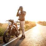 ¿Por qué se apaga mi moto cuando dejo de acelerar? Motociclista parado al lado de su moto en medio de una ruta asfaltada pero desierta