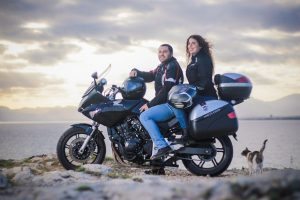 una pareja en moto, sin cascos, mira a la cámara