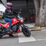 Una mujer con casco rosa se dispone a salir a rodad con una Honda Navi roja