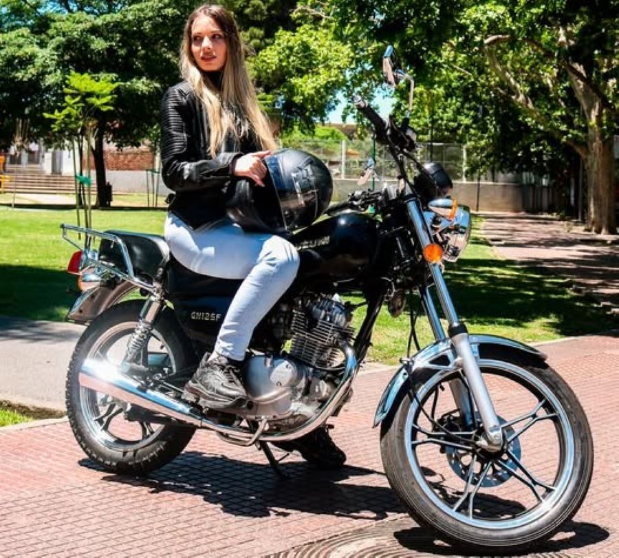 Una joven con ropa informal sostiene su casco sobre una Suzuki GN 125 negra