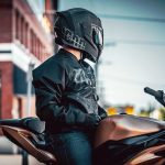 Las mejores marcas de ropa para moto: cuál elegir Un piloto está sentado sobre una motyo naked deportiva con casco y chaqueta Icon negros