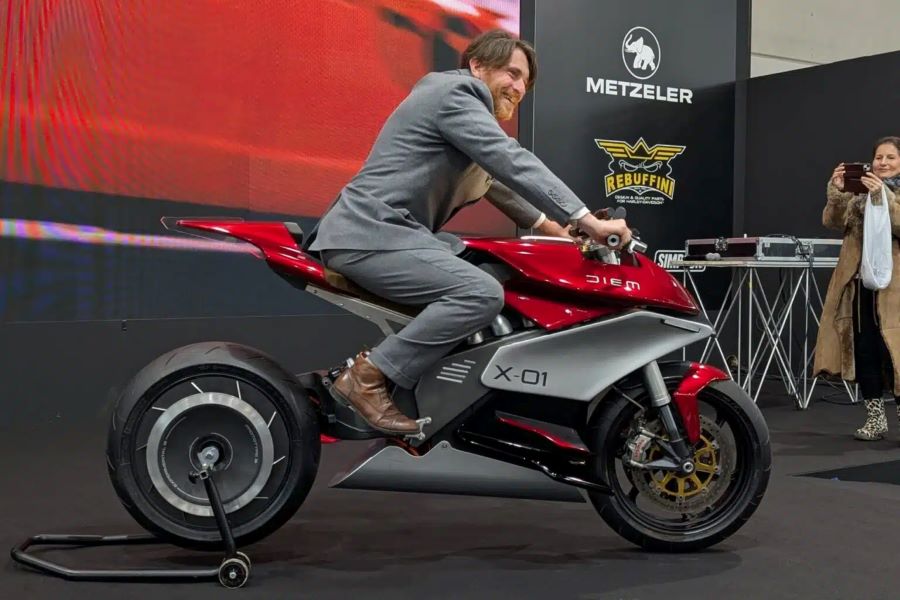 Daniel Kemnitz, líde del proyecto Diem Motors, con traje gris, montado sonriente sobre una X-01 roja y gris