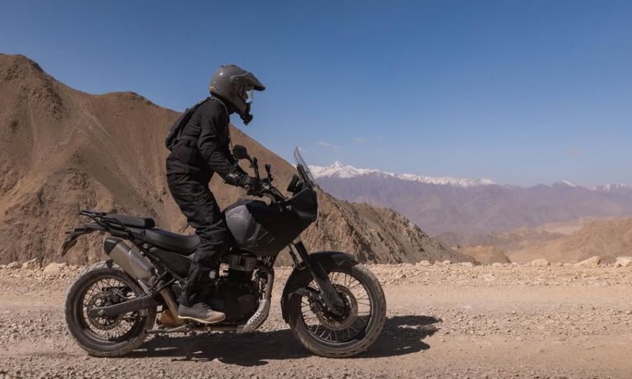 Un piloto con atuendo negro se para sobre las estriberas de un prototipo negro de Himalayan 750 para probar prestaciones de la futuro moto trail