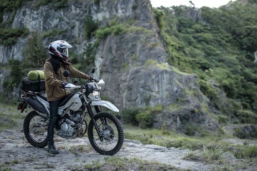 Una usuaria con su Kawasaki KLX230 Sherpa blanca se para a observar el paisaje montañoso
