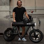 Motos eléctricas disruptivas: diseño, innovación y propósito Un hombre vestido de negro con ropa deportiva y zapatillas blancas sostiene una moto eléctrica Pocket Rocket totalmente negra