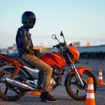 Reglas para conducir moto: todo lo que hay que saber para salir Un motociclista, con casco calzado, sobre una moto naked naranja, espera para comenzar un circuito con conos en una prueba de manejo.