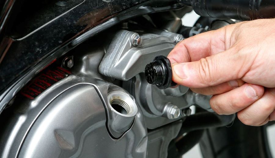 Una mano quita el tapón del reservorio de aceite a una moto de 110 cc