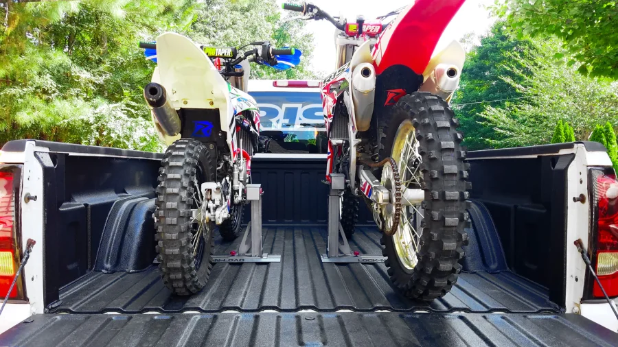Dos motocicletas de cross subidas a la caja de una camioneta y vistas desde atrás.