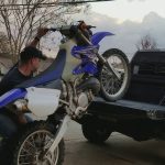 ¿Cómo subir una moto a una camioneta sin rampa? Un hombre intentando subir solo una moto de cross a la caja de una camioneta.