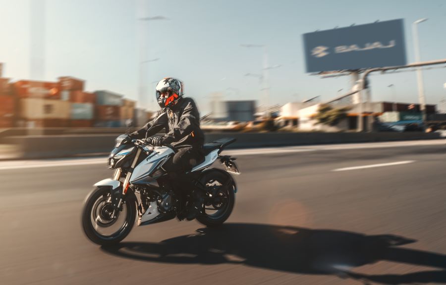 Una Bajaj Rouser N250 UG se tralada por una autopista con un cartel publicitario de la marca en el fondo