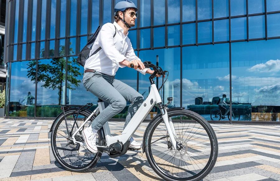 Un hombre con ropa informal, mochila y casco para bibicletas se traslada en una moto bicicleta eléctrica blanca
