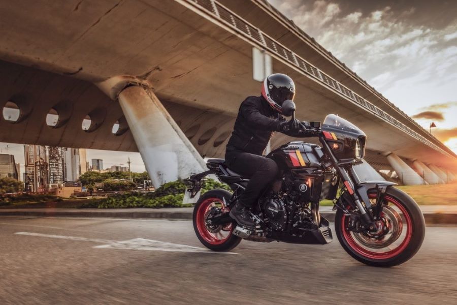 Una Suzuki GSX-8TT oscura y con llantas rojas pasa por debajo de un puente