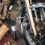 Dos manos enguantadas de un mecánico trabaja en la rueda delantera de una moto