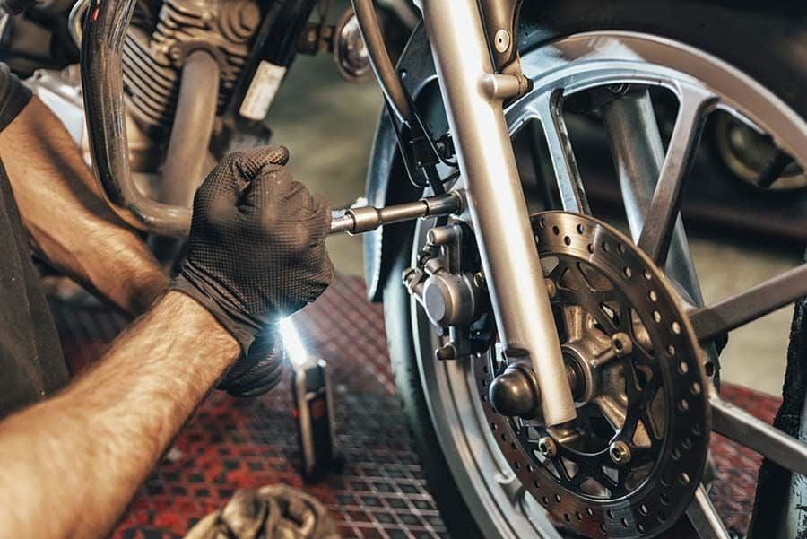 Herramientas para taller de motos: el equipamiento correcto Dos manos enguantadas de un mecánico trabaja en la rueda delantera de una moto