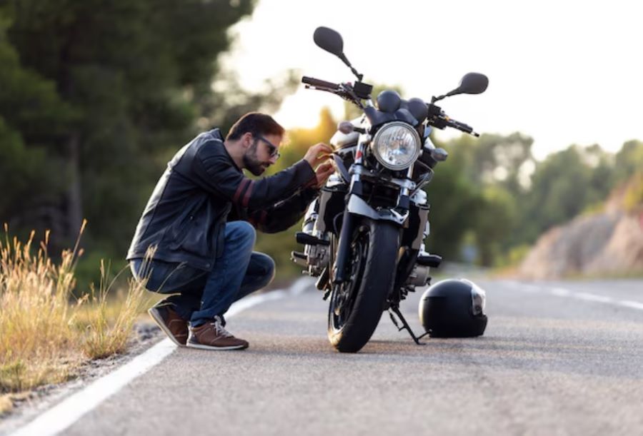 arreglando moto en ruta Una persona en cuclillas examina el motor de una moto en plena ruta