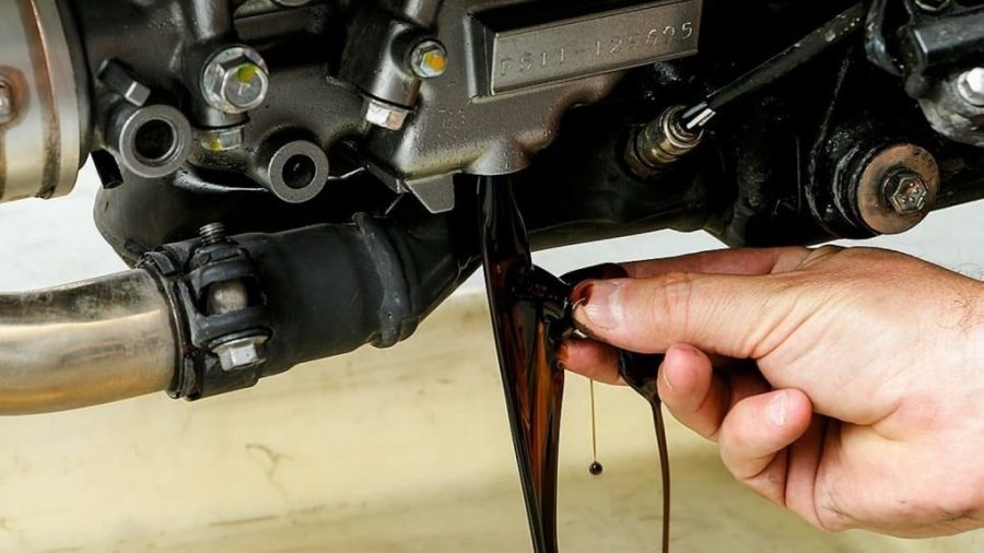 Una mano quita el tapón del tanque de aceite de una moto para hacer el recambio y el líquido fluye oscuro
