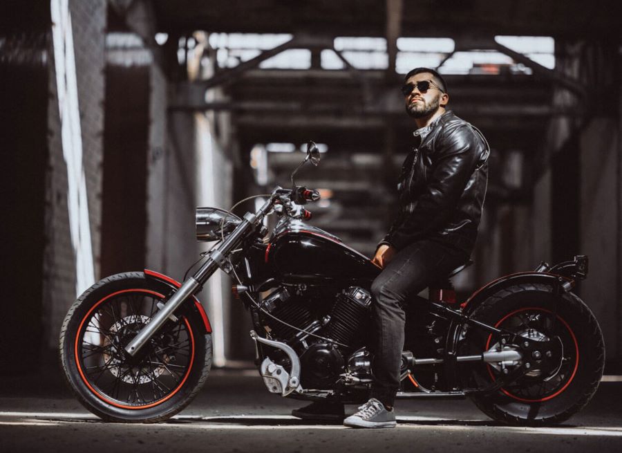 moto chopper personalizada Un motociclista con lentes y campera negra de cuero sentado sobre una moto chopera al tono