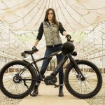 Moto Bicicleta: ¿Qué es, cómo funciona y cuál conviene elegir? Una mujer posa detrás de su moto bicicleta eléctrica negra tipo mountain bike
