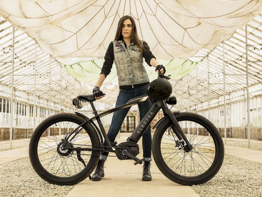 Una mujer posa detrás de su moto bicicleta eléctrica negra tipo mountain bike