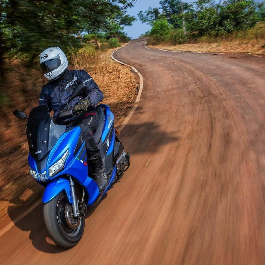 Una Aprilia SXR160 azul en acción sobre una ruta boscosa