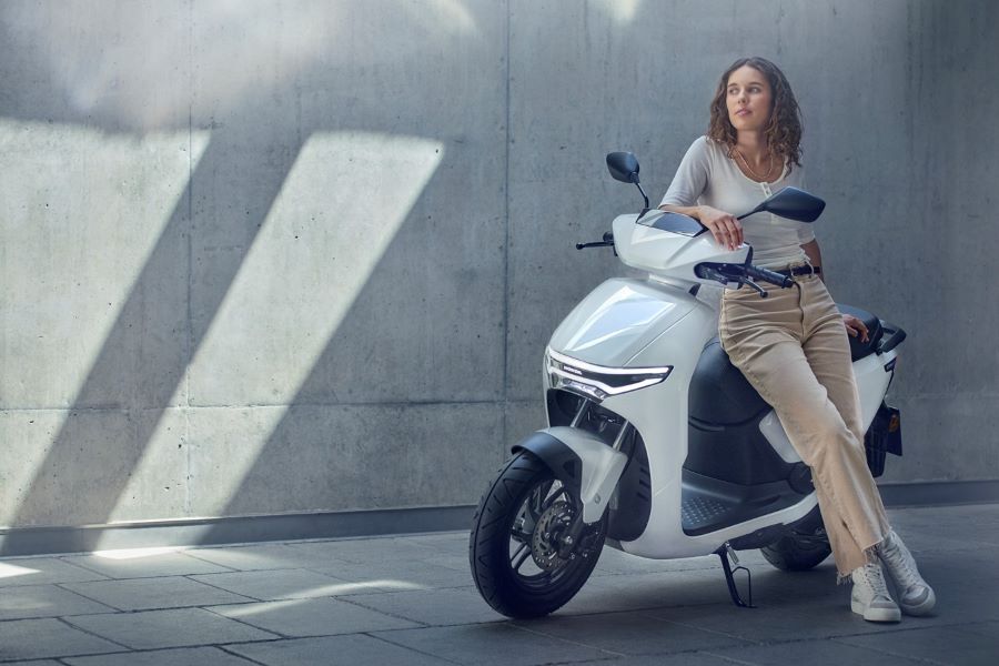 Una modelo rubia recostada sobre un scooter Honda CUV e blanco