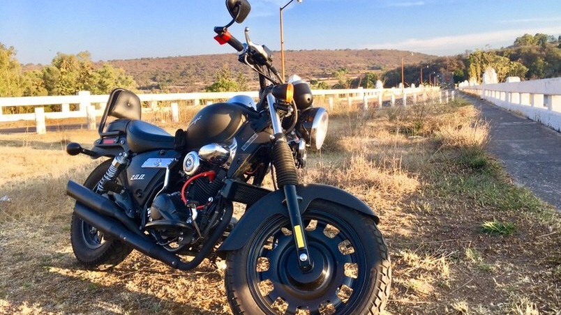Una Kewway Superlight negra parada detrás de una valla blanca a un costado de la ruta de una zona campestre