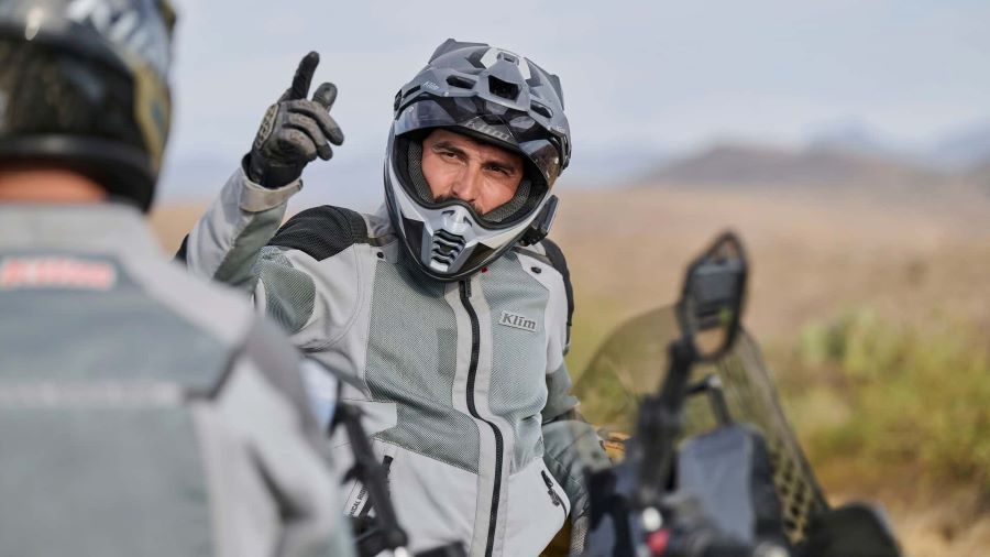 Un motociclistas con una chaqueta Klim gris y casco conversa con otro de moto a moto