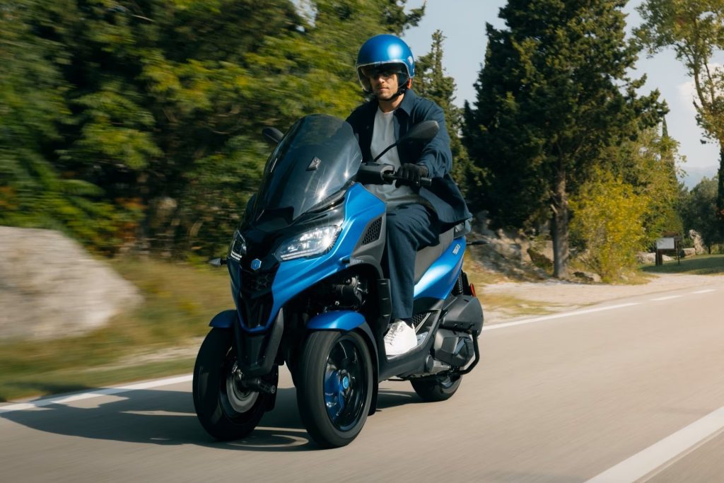 Un piloto viaja en un Piaggio MP3 300 azul en un contexto rutero