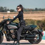Una mujer está sentada sobre una moto custom SRV 600 gris de QJMotor en un paisaje rural